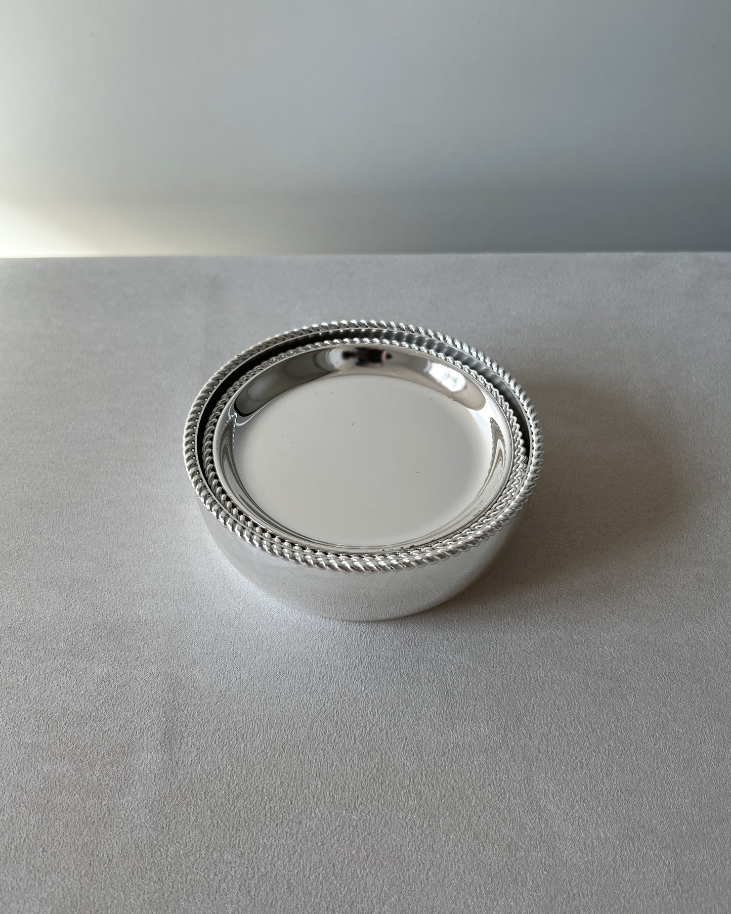 Six silver-plated drink coasters by BBI Prasent stacked neatly inside the matching tall wine bottle coaster, showcasing the set's elegant design.