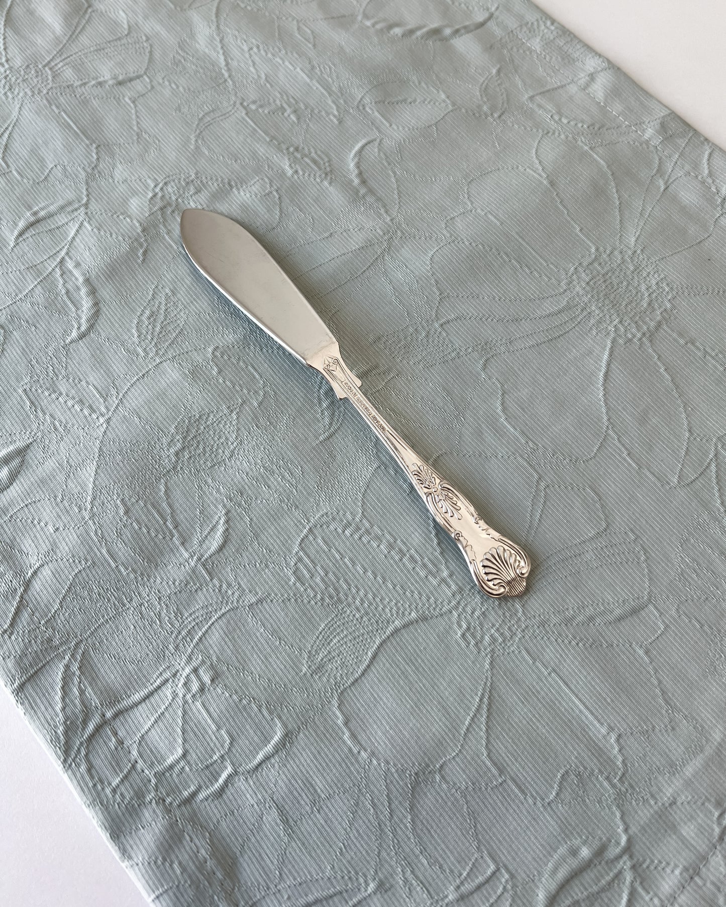 The seashell butter knife shown alongside other antique silverware to demonstrate its place within an esteemed collection of English heritage pieces.