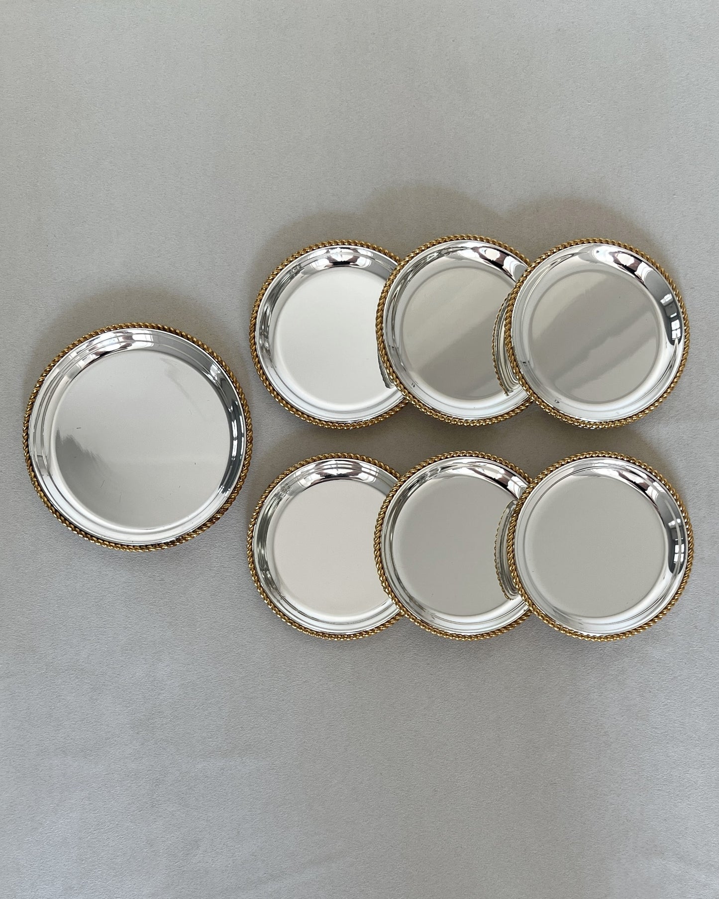 Set of seven vintage BBI Präsent drink coasters and wine bottle coaster, each featuring a silver-plated base and a glamorous gold-plated twisted rope rim for a two-tone effect.