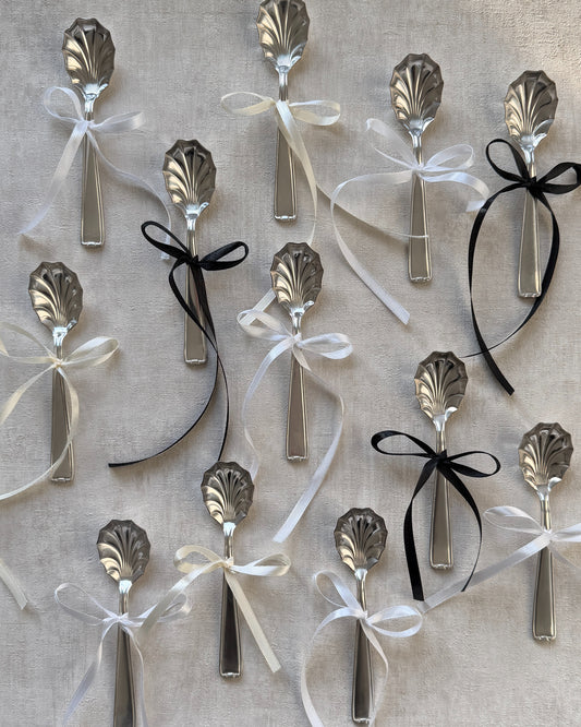 A group of vintage Michelin silver-plated shell serving spoons tied with decorative bows, showcasing them as perfect holiday or host gifts.