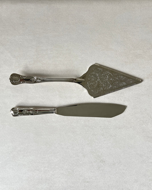 Close-up of the ornate handles with raised seashell detailing on the mid-century silver-plated cake knife and server.