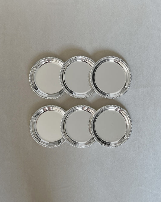 Six vintage mid-century silver-plated drink coasters arranged on a tabletop, ready for entertaining and protecting surfaces with timeless style.