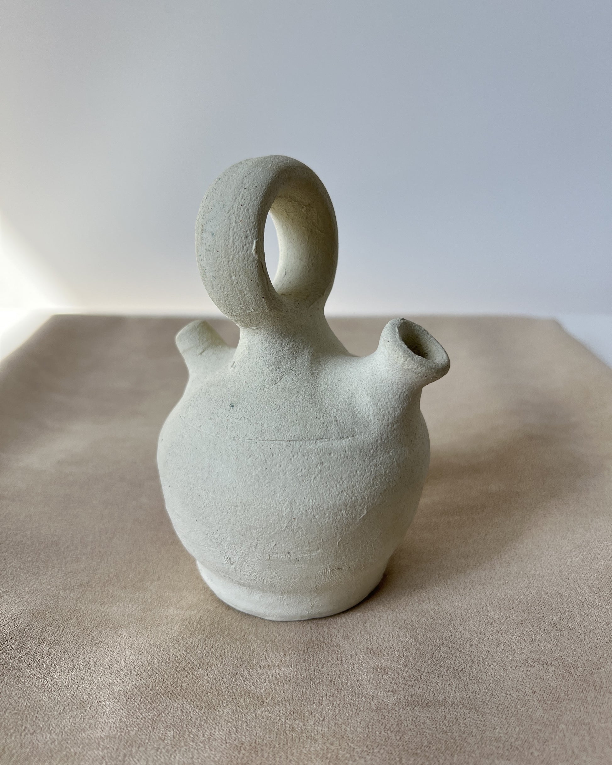 Mini vintage Spanish botijo water jug made of unglazed natural clay from the 1970s, showcased front-on against a white background, highlighting its bulbous body, narrow spout, and traditional Búcaro design for cooling water naturally.
