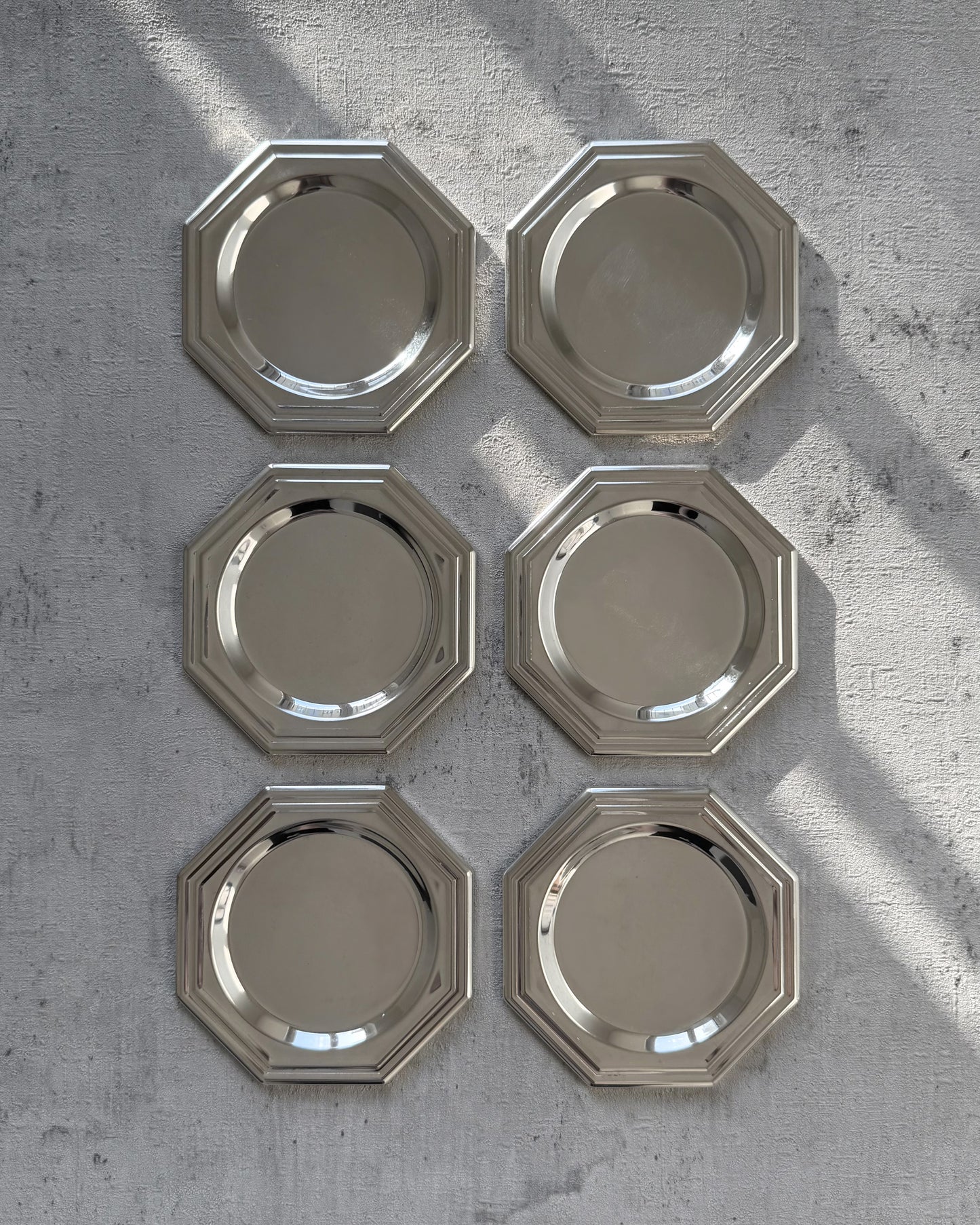 A complete set of six minimalist 1980s octagonal silver-plated coasters with a sleek, reflective mirror finish, arranged to show their unique geometric silhouette.