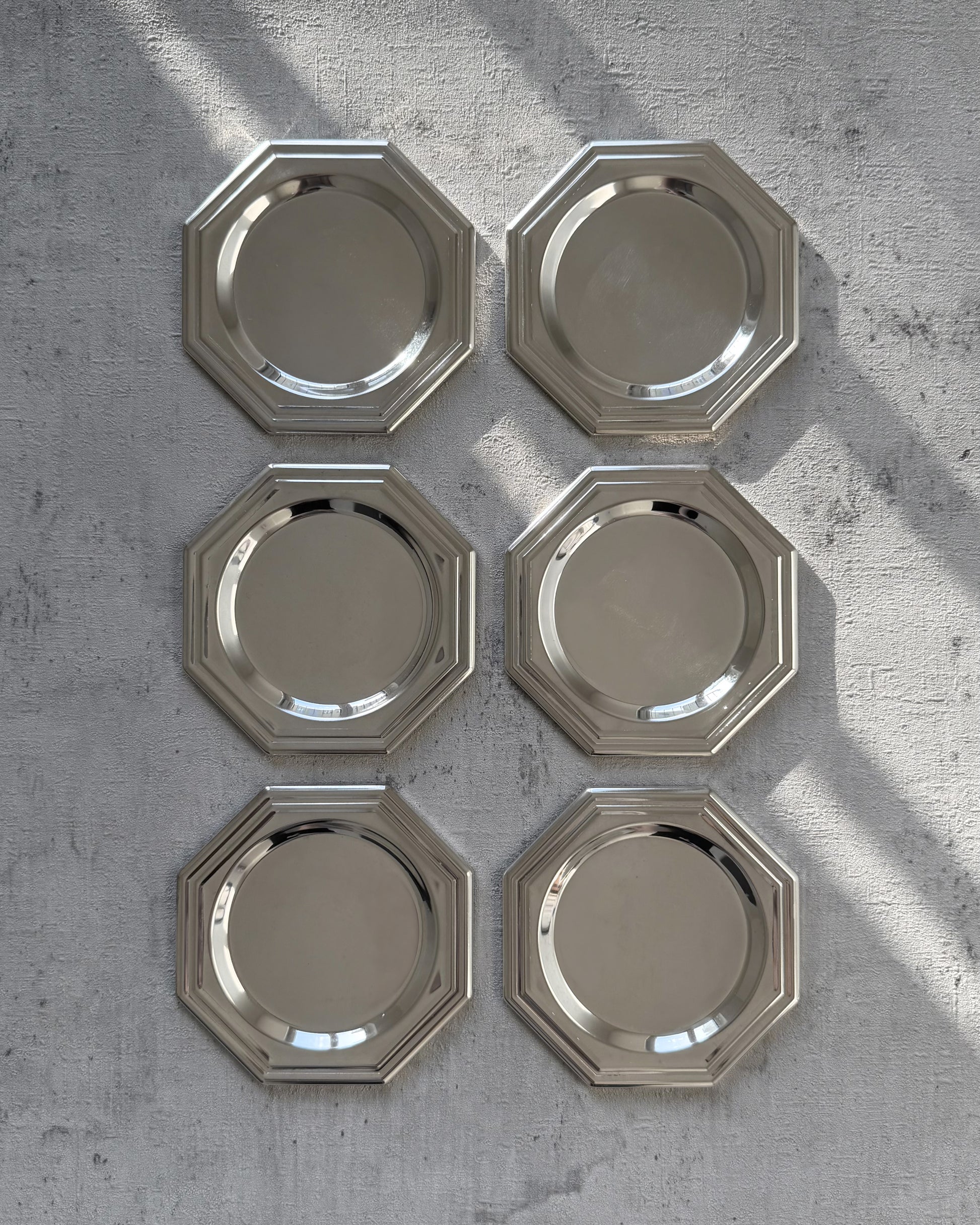 A complete set of six minimalist 1980s octagonal silver-plated coasters with a sleek, reflective mirror finish, arranged to show their unique geometric silhouette.