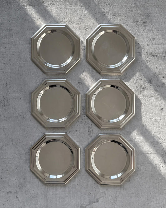 A complete set of six minimalist 1980s octagonal silver-plated coasters with a sleek, reflective mirror finish, arranged to show their unique geometric silhouette.