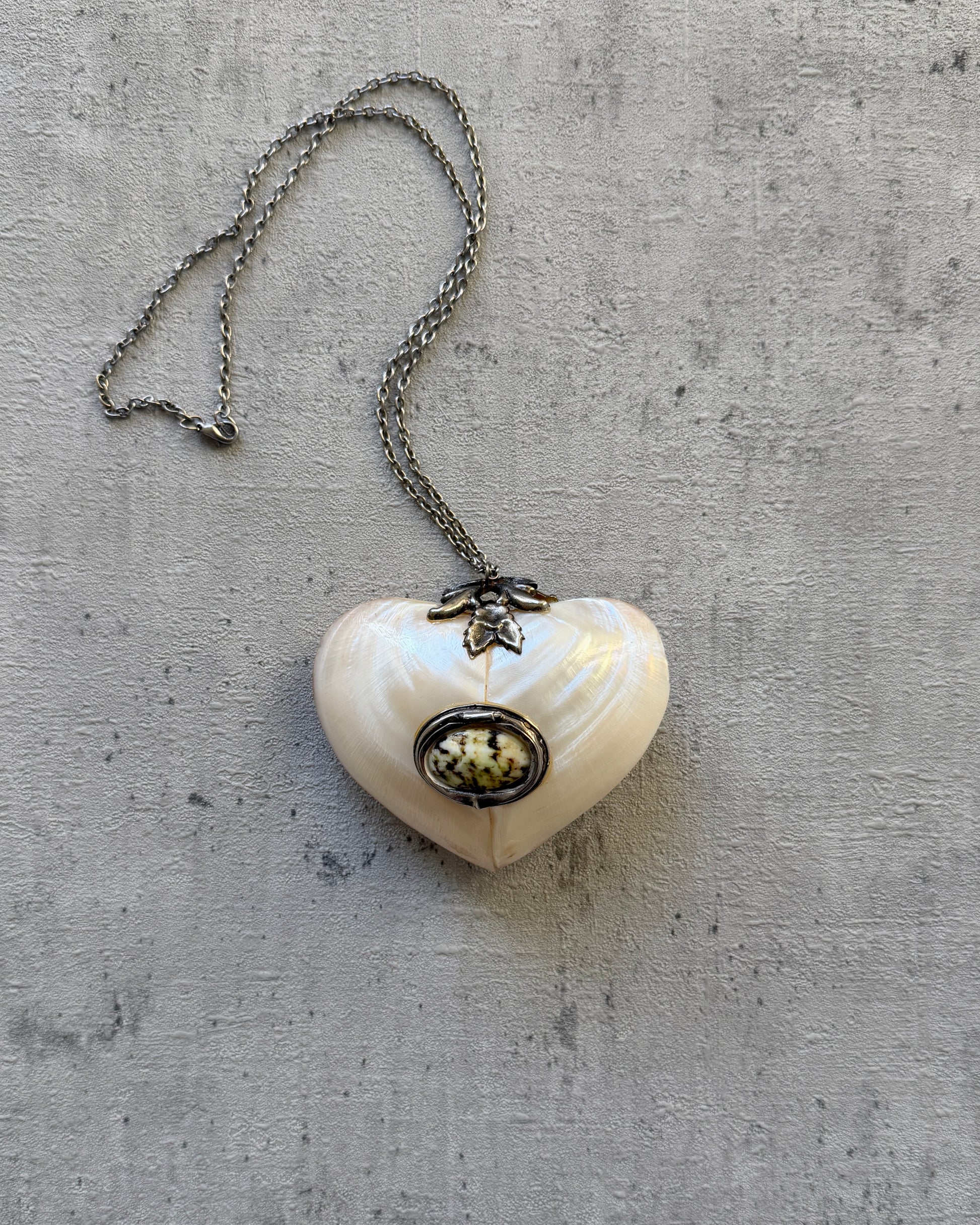 A full view of the antique mother-of-pearl heart locket suspended on a delicate chain, displayed against a neutral white background.