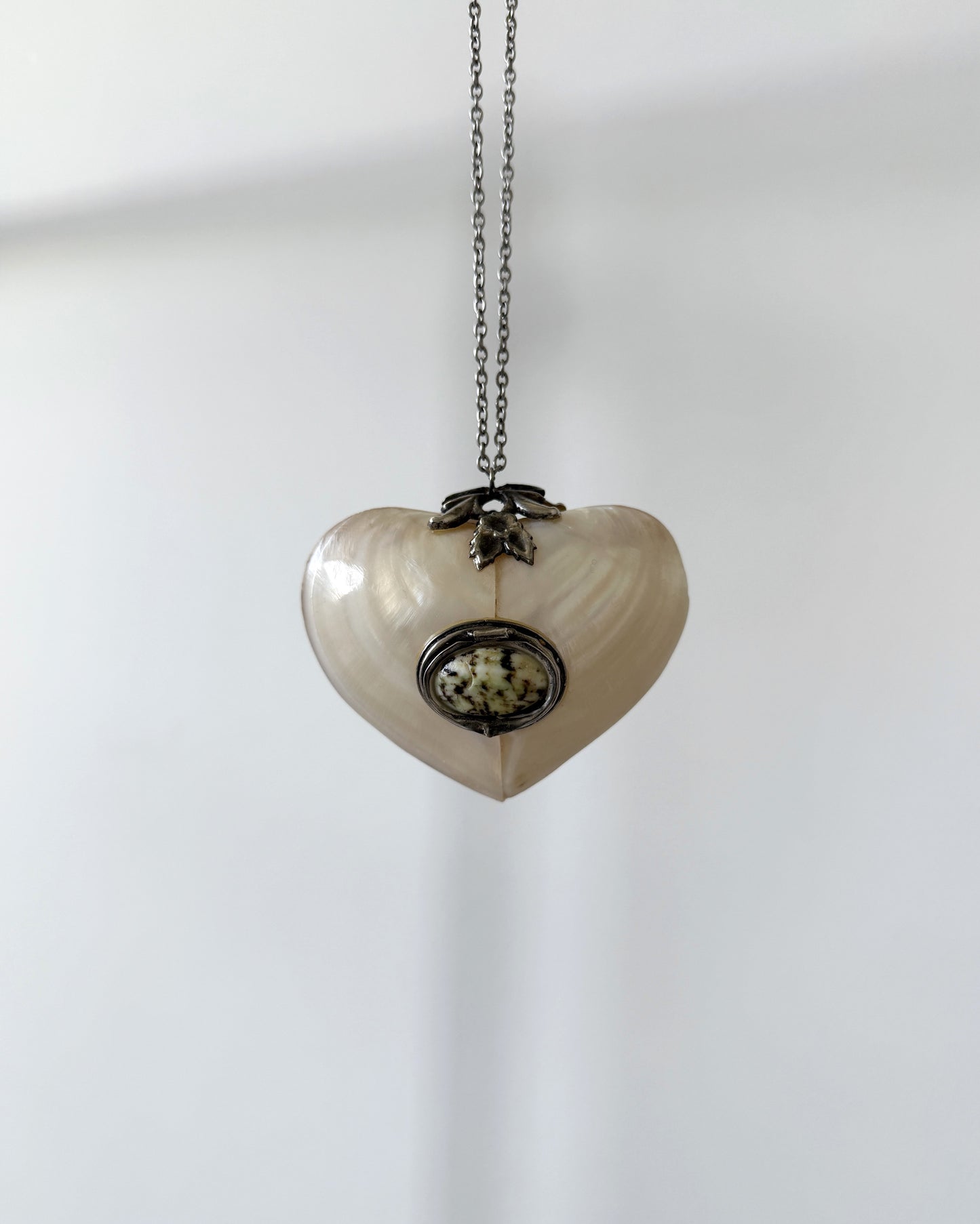 A full view of the antique mother-of-pearl heart locket suspended on a delicate chain, displayed against a neutral white background.