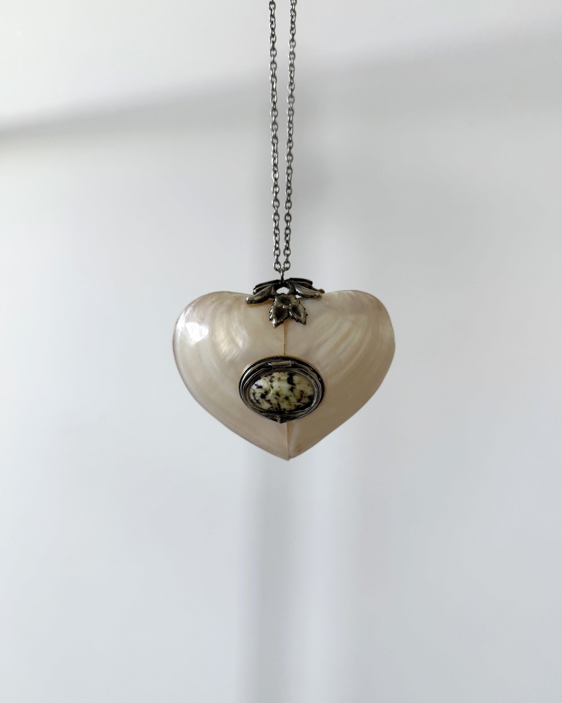 A full view of the antique mother-of-pearl heart locket suspended on a delicate chain, displayed against a neutral white background.