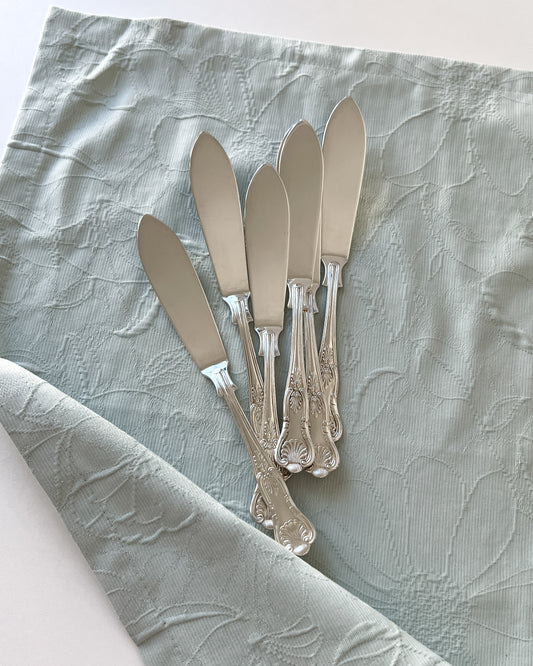 A full view of an antique Sheffield silver-plated butter knife, showcasing its slender blade and elegant seashell motif handle.