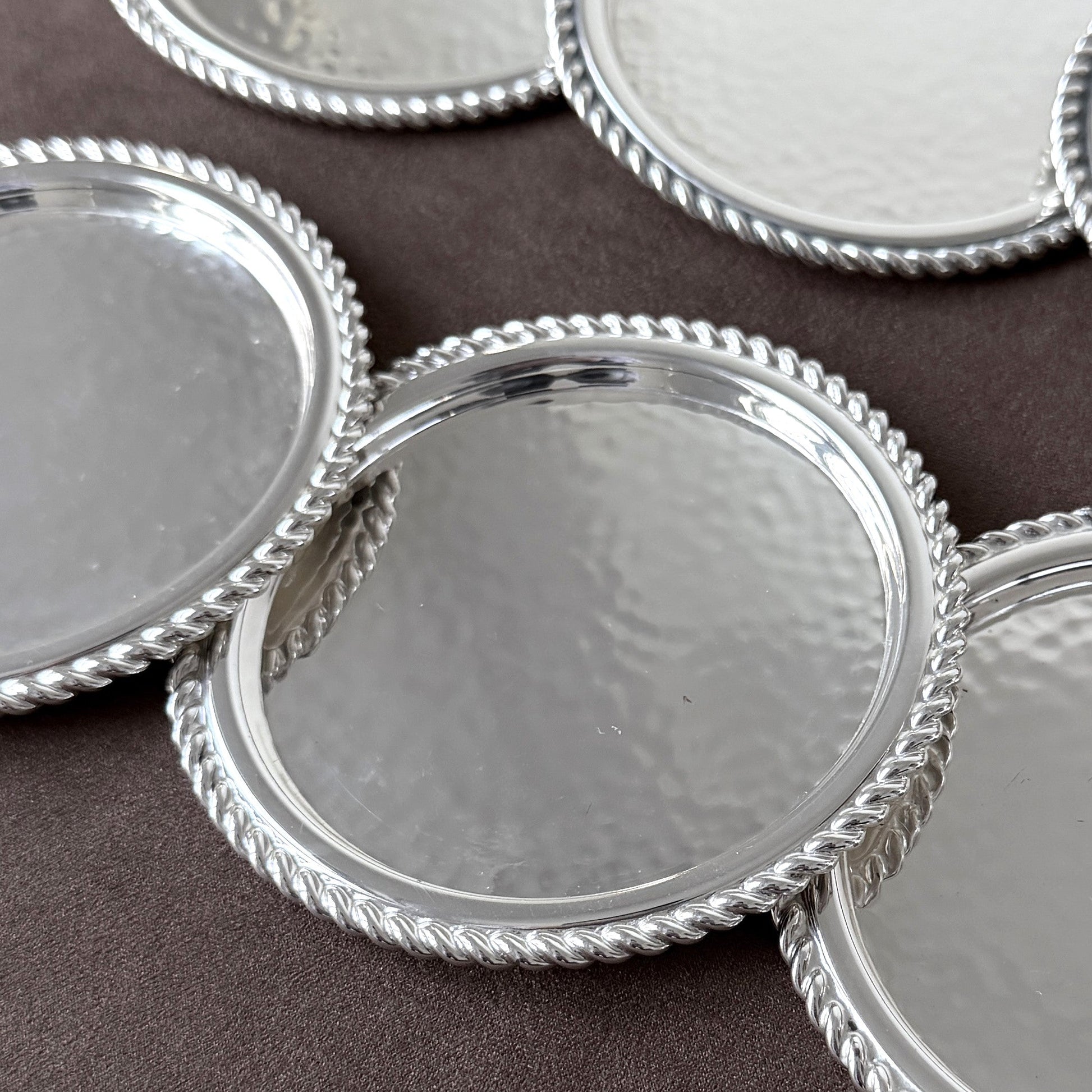 Close-up detail of the artisan hammered silver-plated texture and meticulously detailed twisted rope rim on a mid-century German drink coaster.