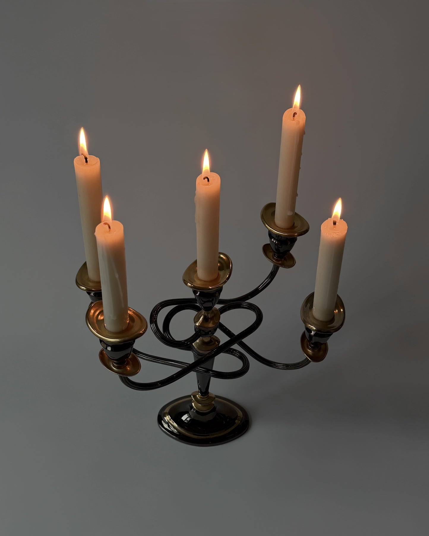 A detailed close-up of the burning candles on the twisted metal arms, highlighting the atmospheric contrast of the dark bronze-toned finish.