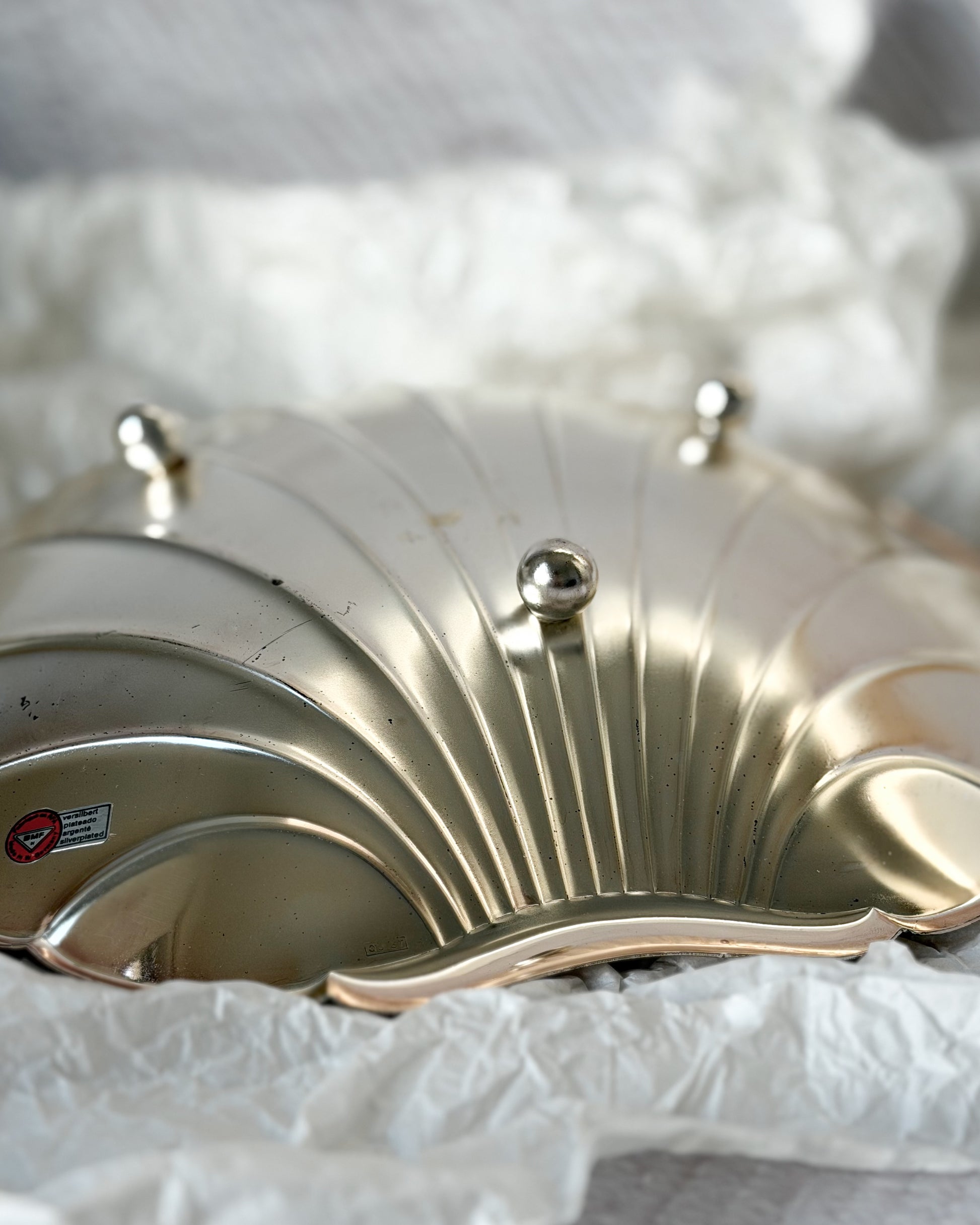 A side profile of the mid-century silver shell centerpiece, showing the three elegant ball-legs that support the substantial sculptural tray.