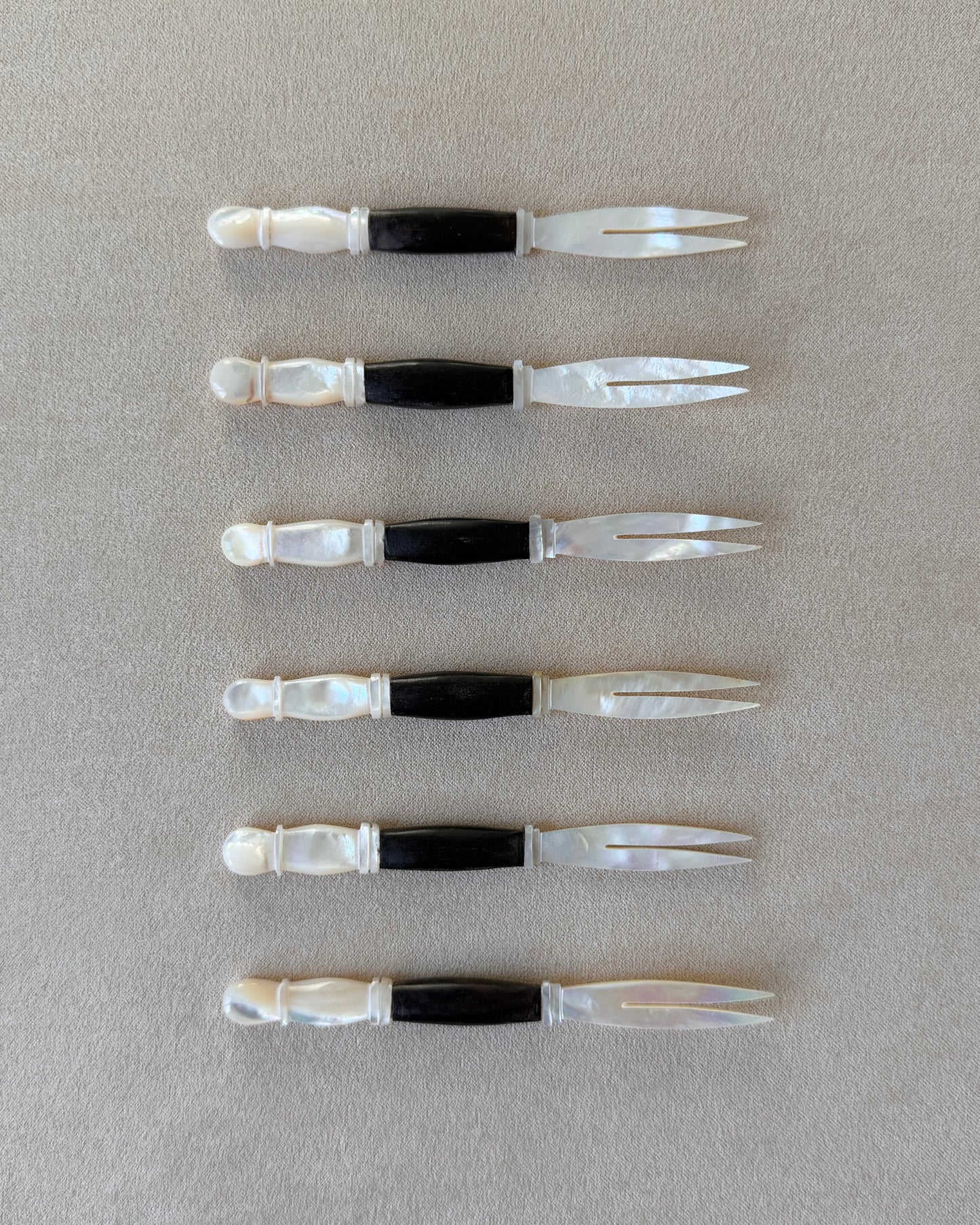 A mid-century modern appetizer fork featuring a hand-carved dark teak wood handle and a luminous mother-of-pearl head, isolated on a neutral background.