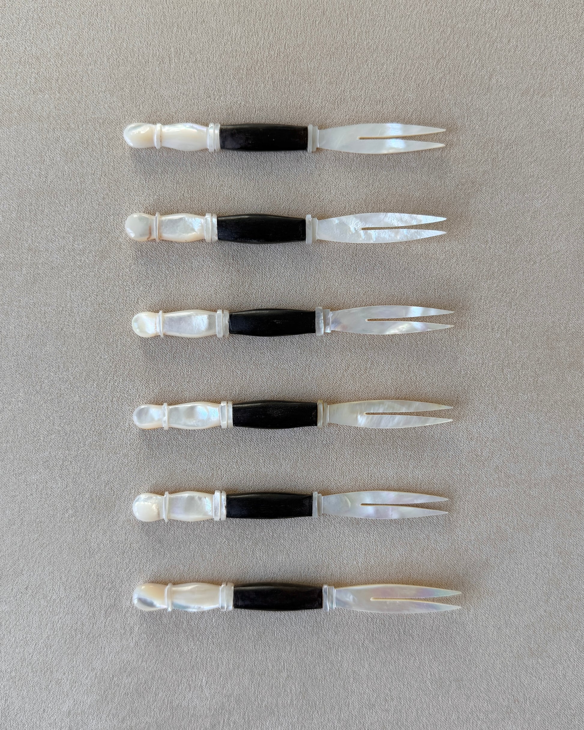 A mid-century modern appetizer fork featuring a hand-carved dark teak wood handle and a luminous mother-of-pearl head, isolated on a neutral background.