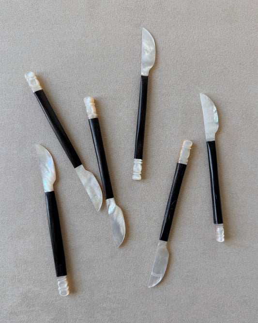 A mid-century modern caviar and butter knife featuring a hand-carved espresso teak handle and a luminous mother-of-pearl shell blade.