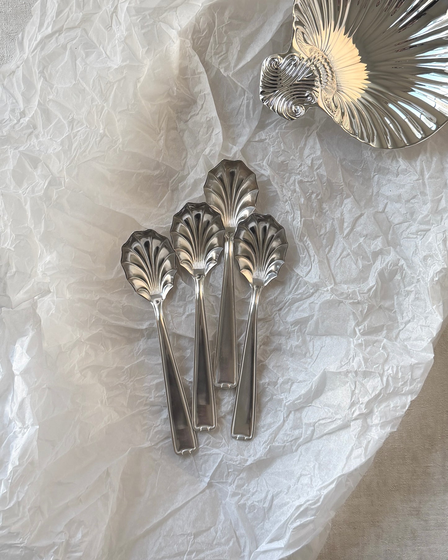 Four German mid-century silver-plated shell spoons arranged with a decorative silver shell on a clean white background.