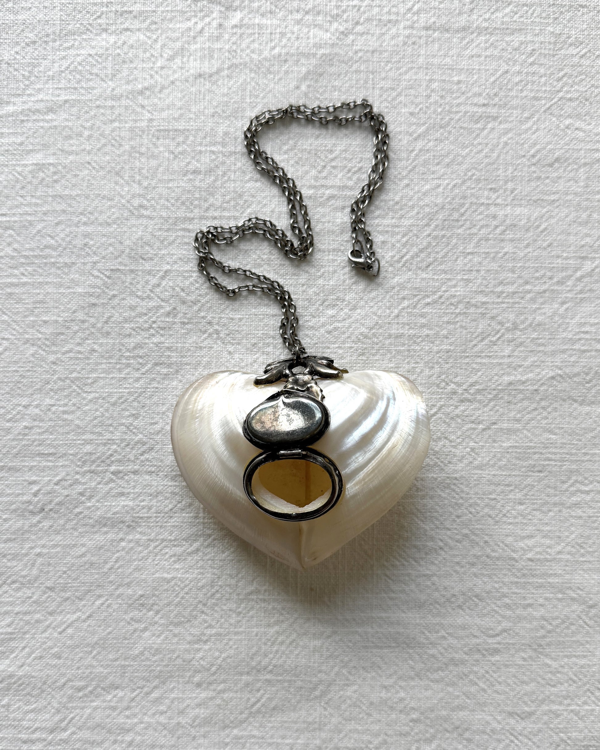 The heart-shaped locket necklace opened to reveal a private storage compartment, demonstrating its function as a chic pill box or keepsake holder.