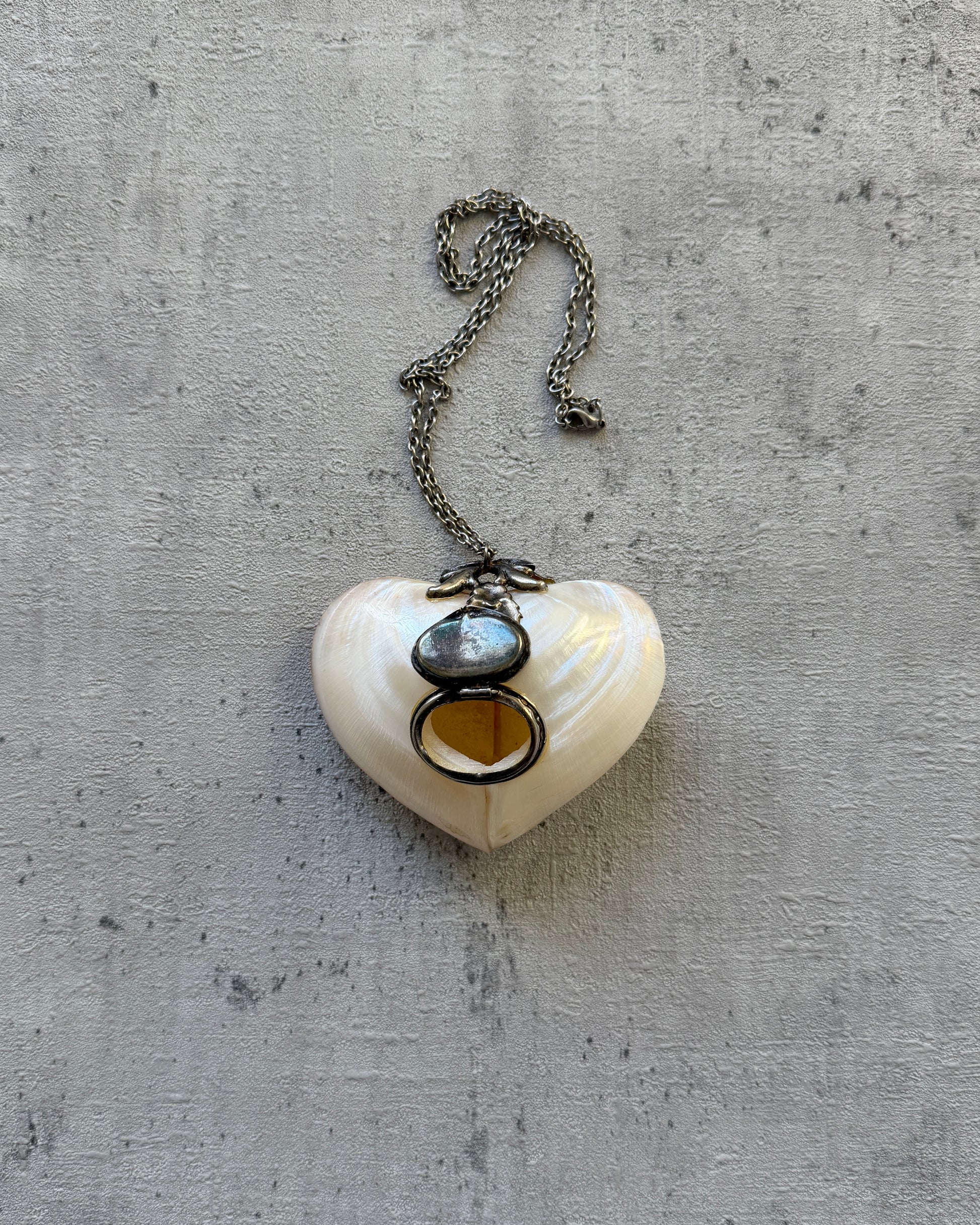 The heart-shaped locket necklace opened to reveal a private storage compartment, demonstrating its function as a chic pill box or keepsake holder.