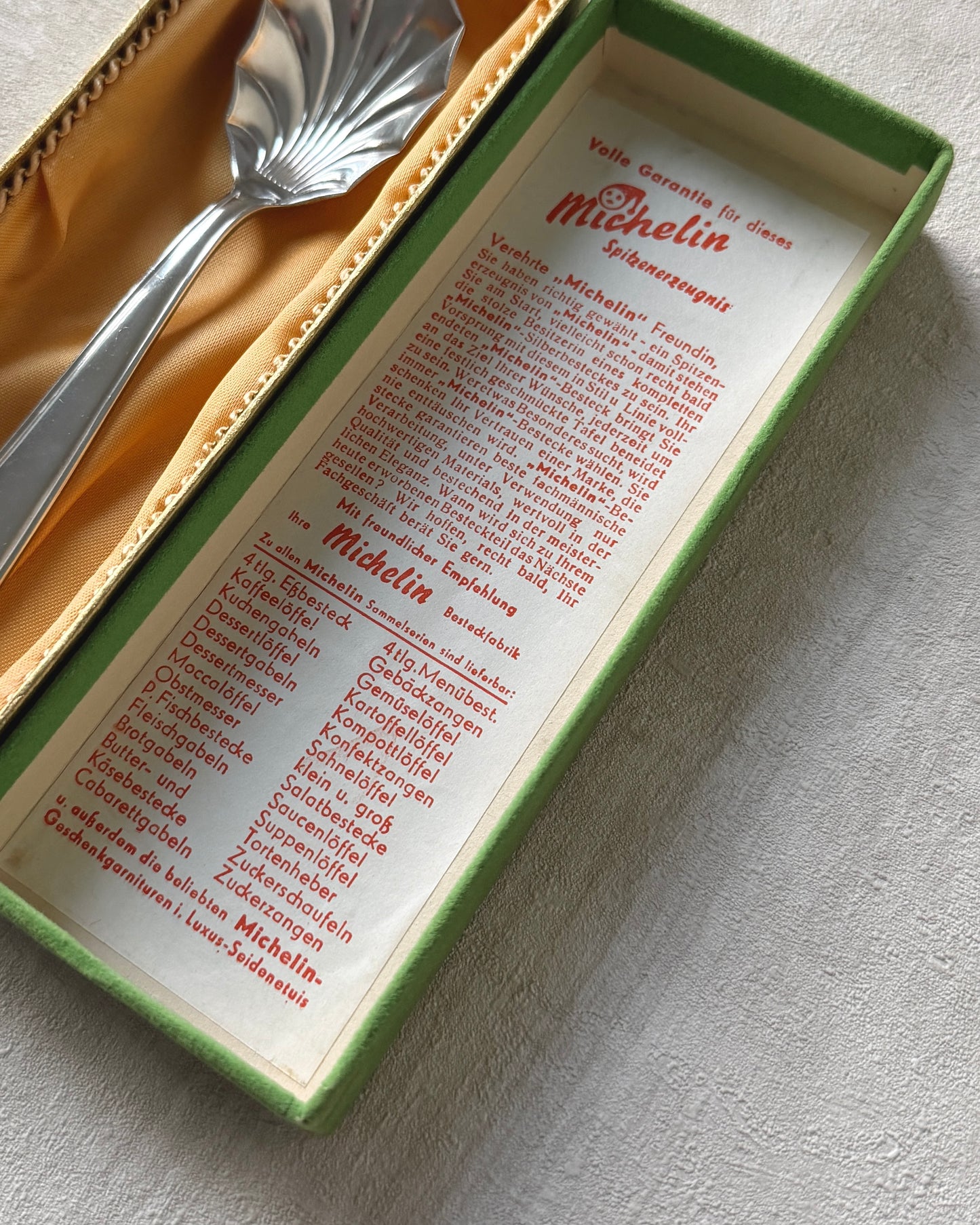 Close-up view of the Michelin shell serving spoon inside its original 1960s packaging, highlighting the pristine condition of the silver plate.