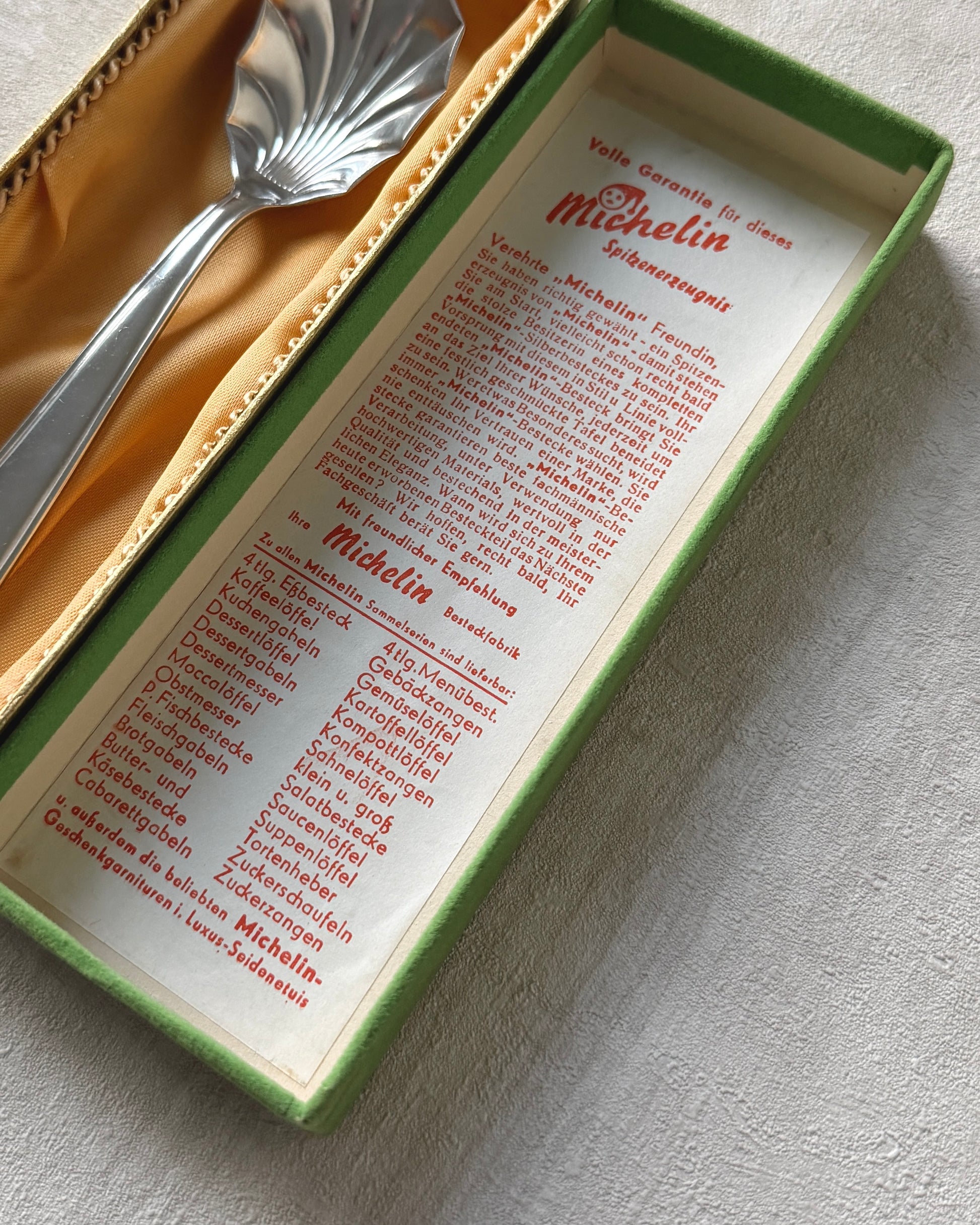 Close-up view of the Michelin shell serving spoon inside its original 1960s packaging, highlighting the pristine condition of the silver plate.
