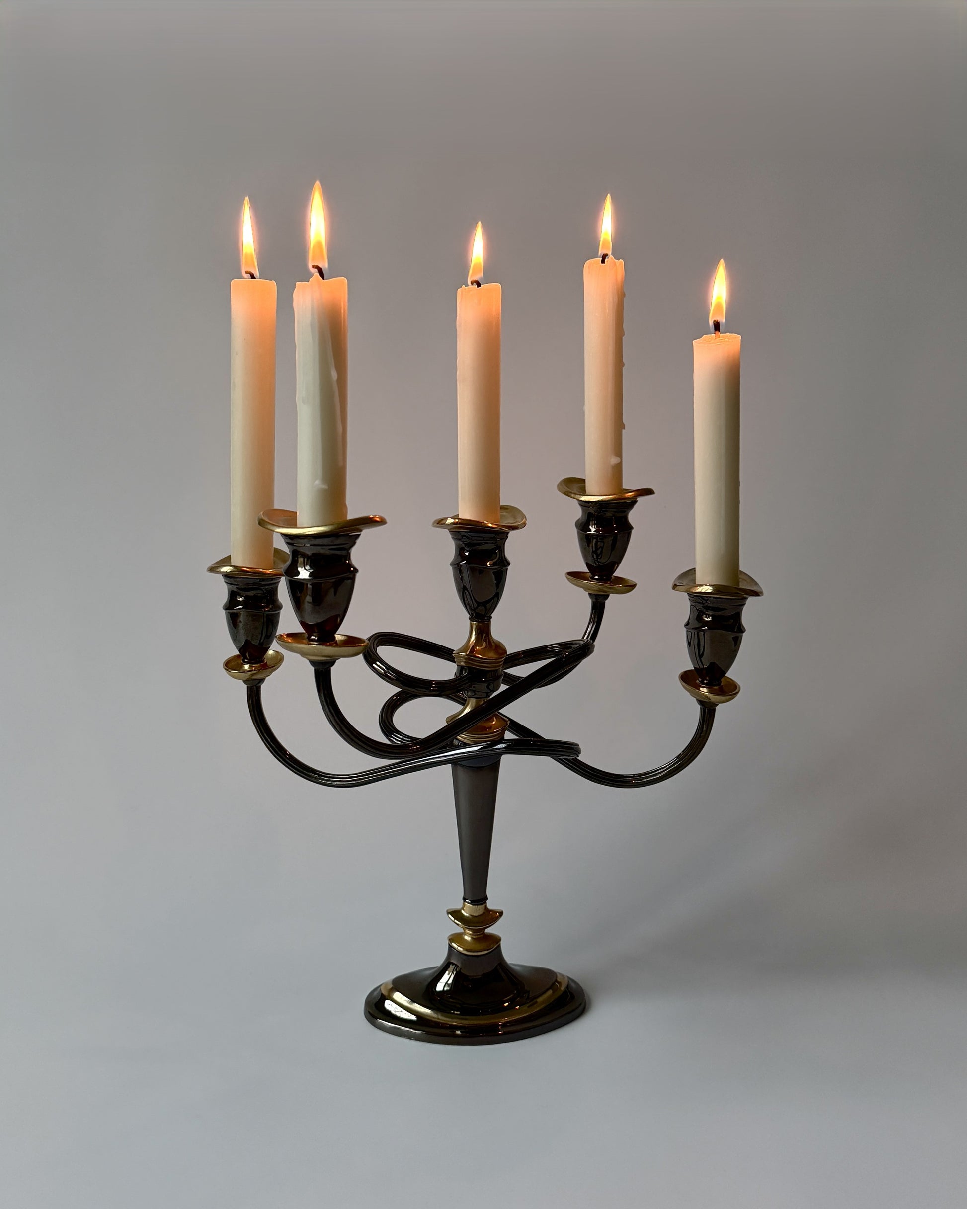 The five-arm twisted metal candelabra with lit taper candles, demonstrating how the flames catch the flicker of the warm gold plating.