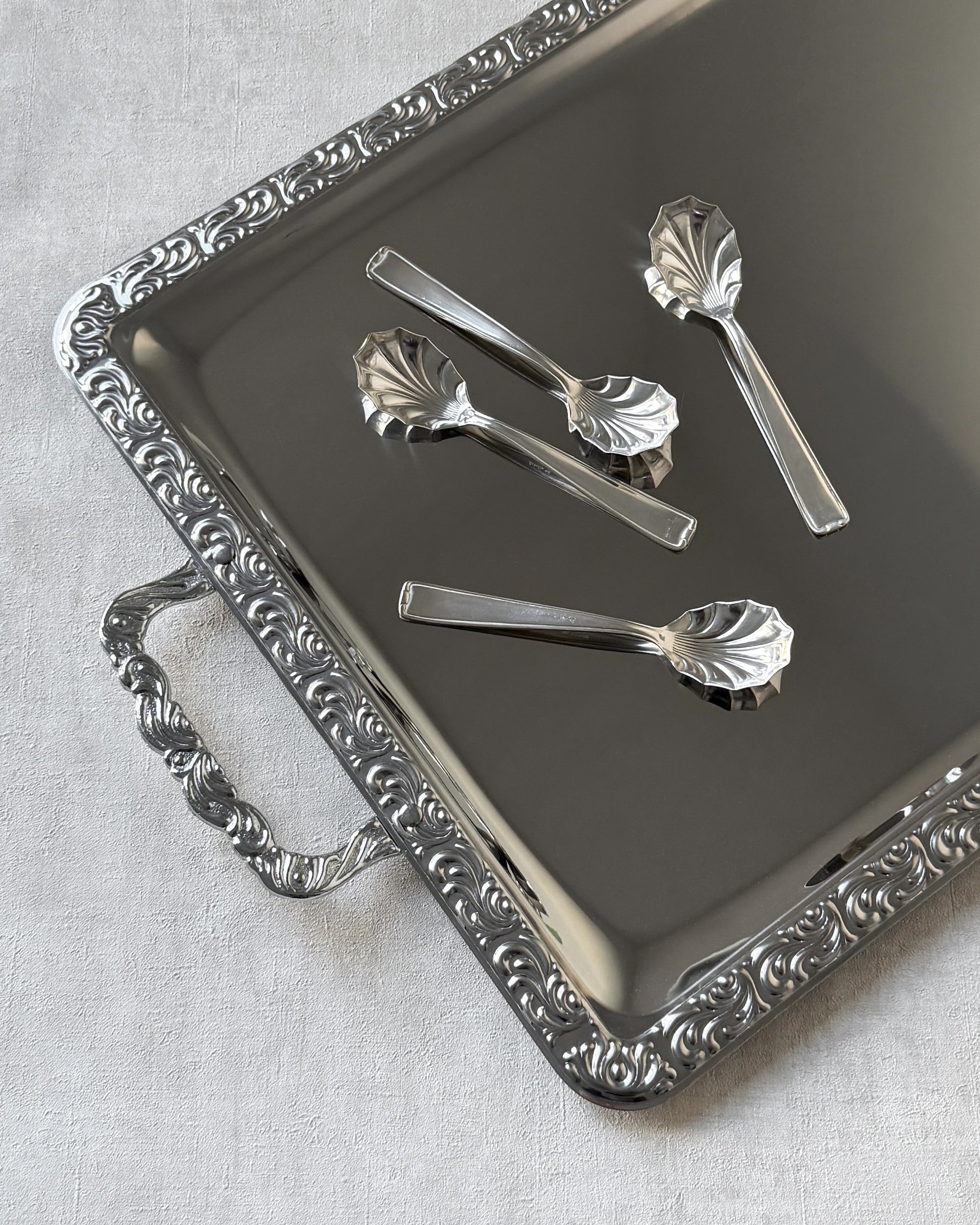 Four silver-plated shell-shaped serving spoons by Michelin Besteckfabrik displayed on an elegant silver serving tray.