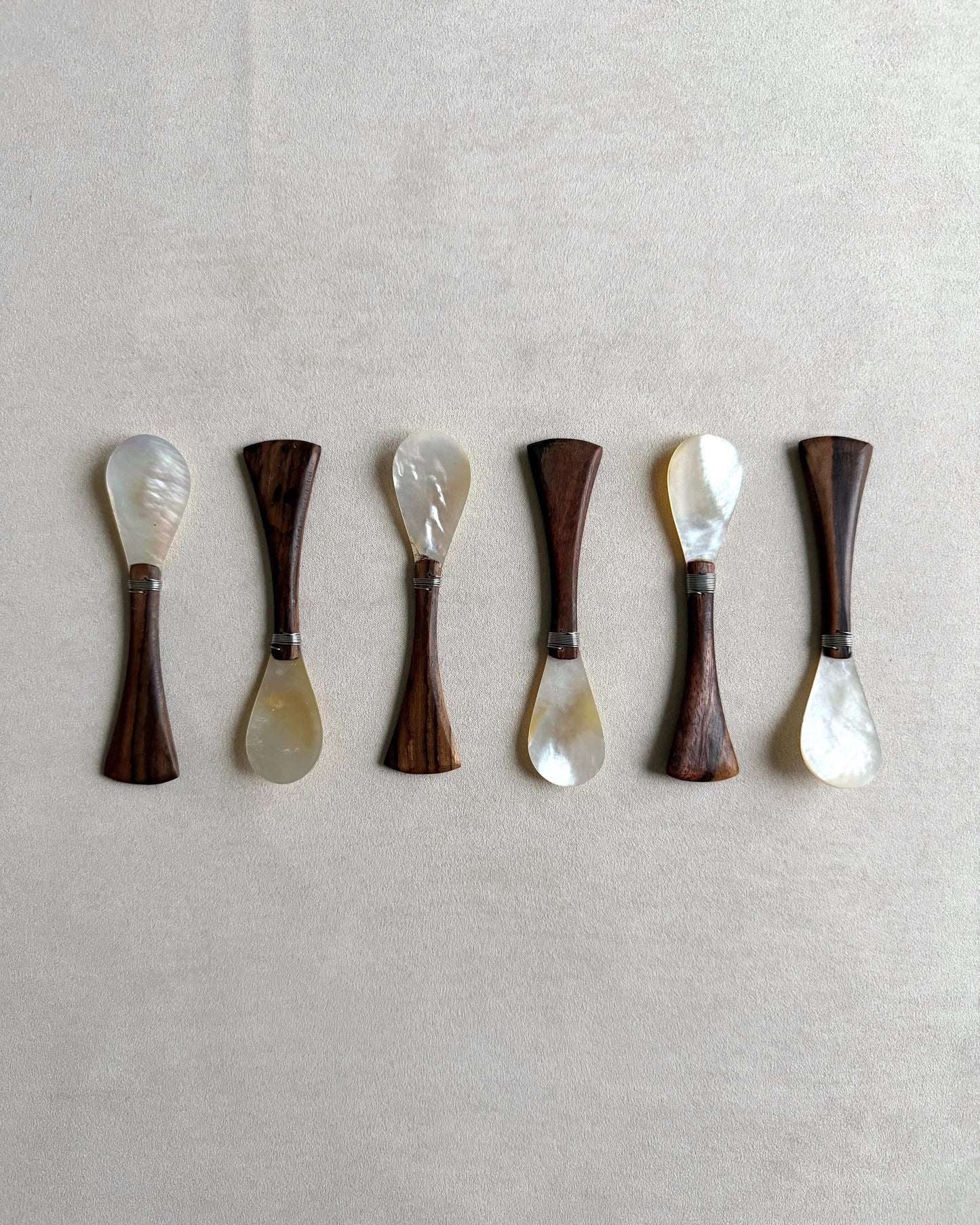 A complete set of six small teak and mother-of-pearl spoons, ideal for use as elegant salt spoons, honey servers, or luxury condiment accessories.