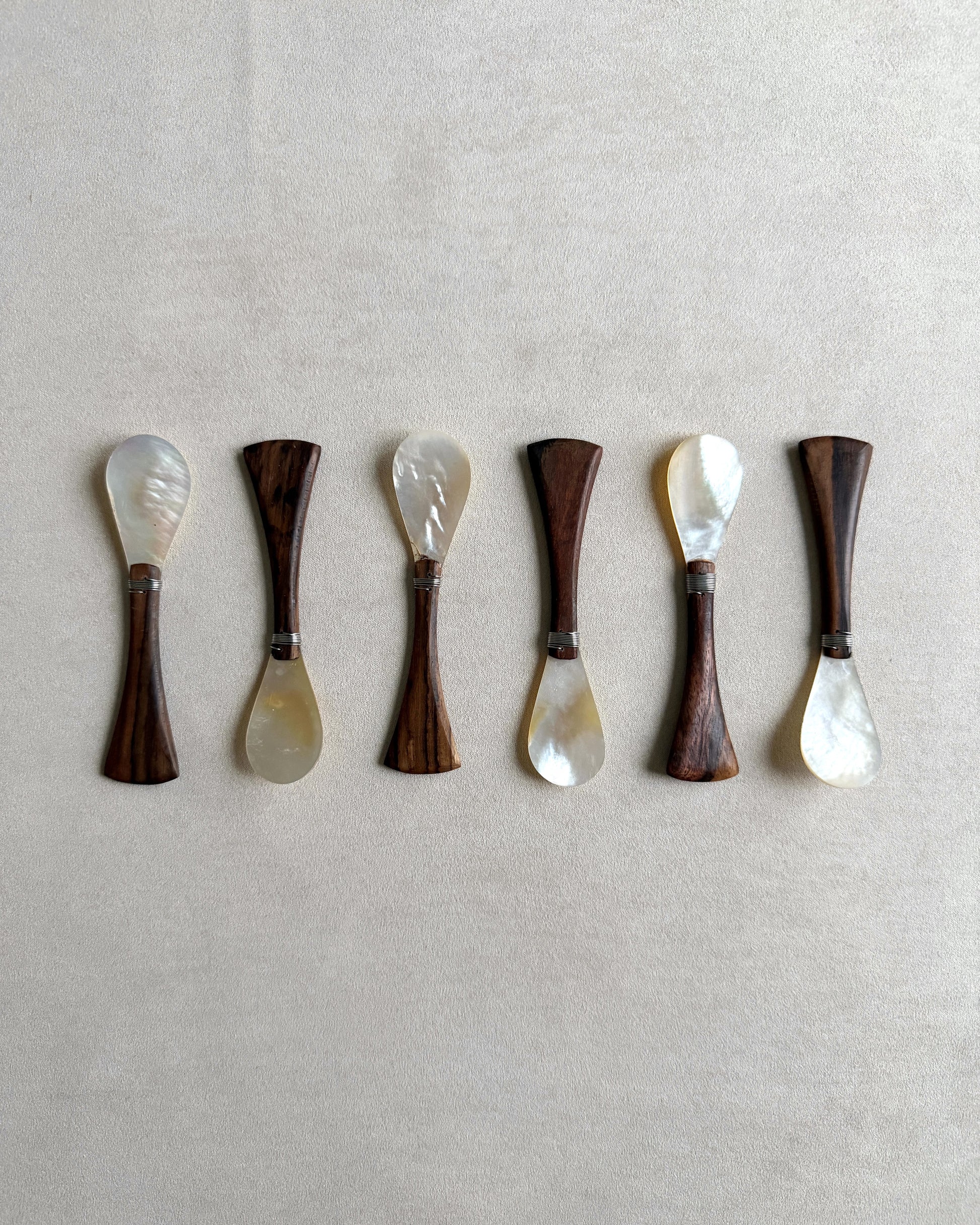 A complete set of six small teak and mother-of-pearl spoons, ideal for use as elegant salt spoons, honey servers, or luxury condiment accessories.