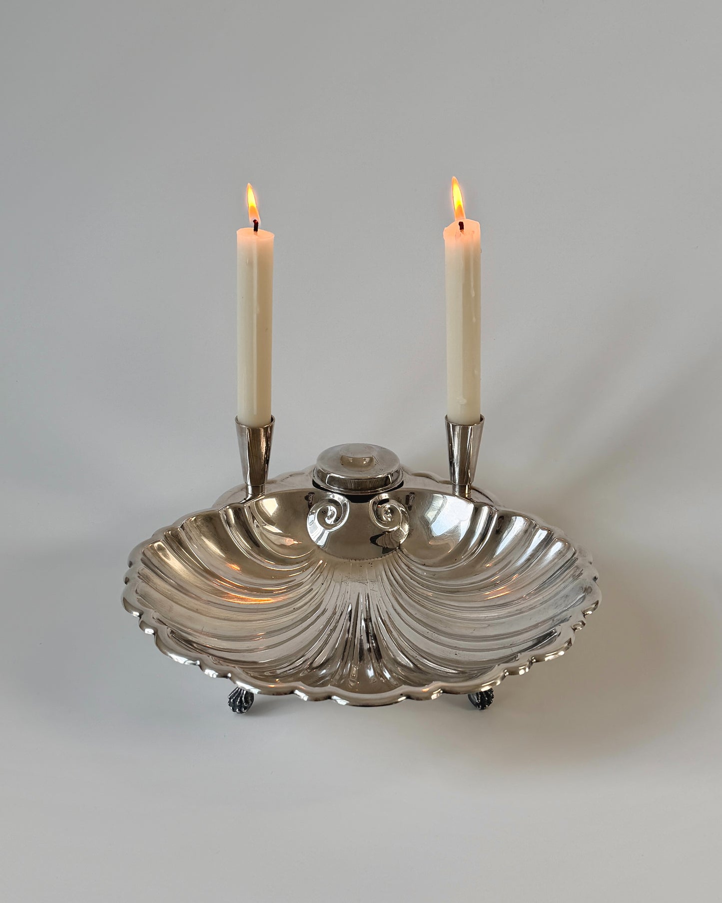 A large vintage Sheffield silver-plated scallop shell centerpiece bowl featuring two integrated taper candle holders and four dainty feet.