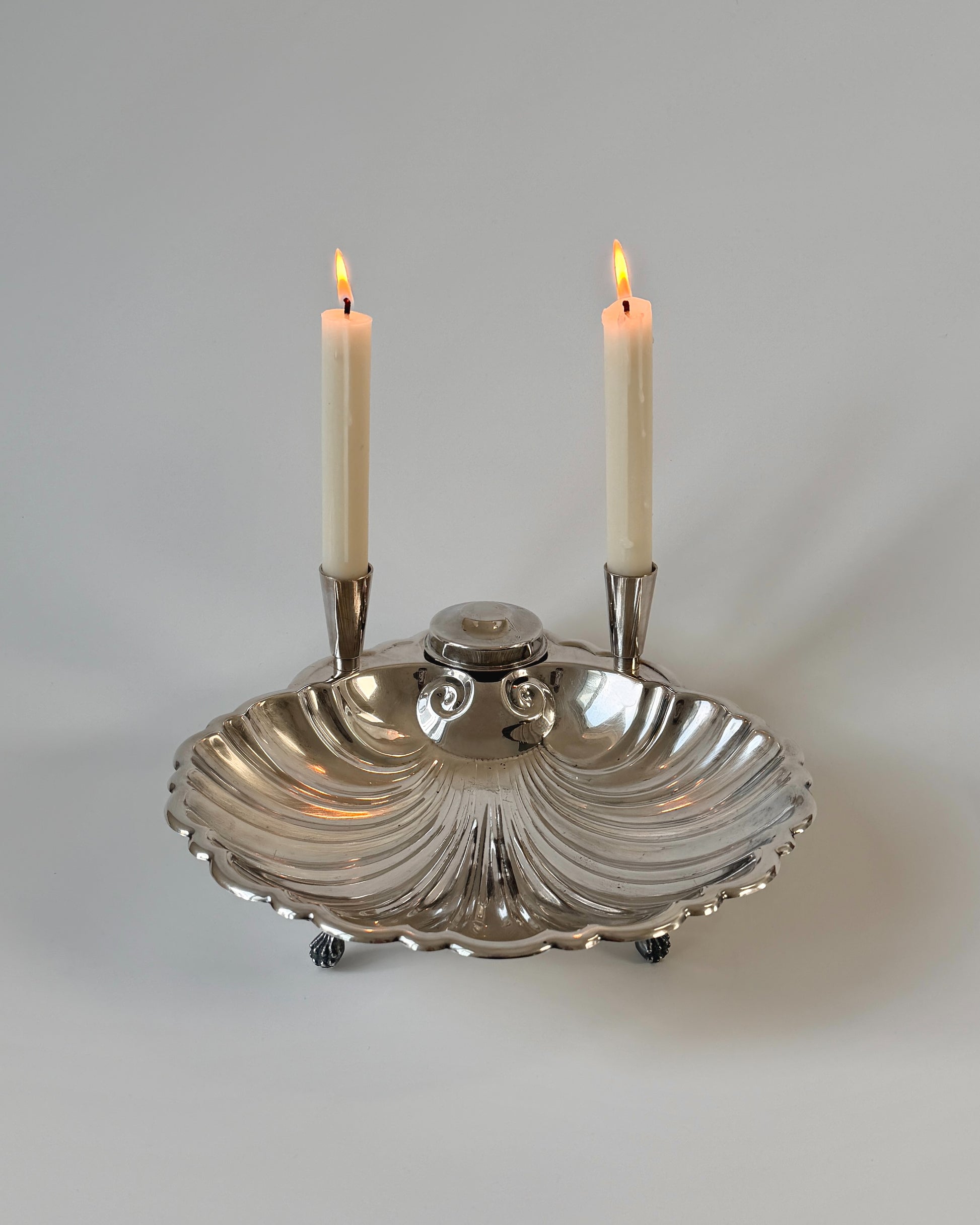 A large vintage Sheffield silver-plated scallop shell centerpiece bowl featuring two integrated taper candle holders and four dainty feet.