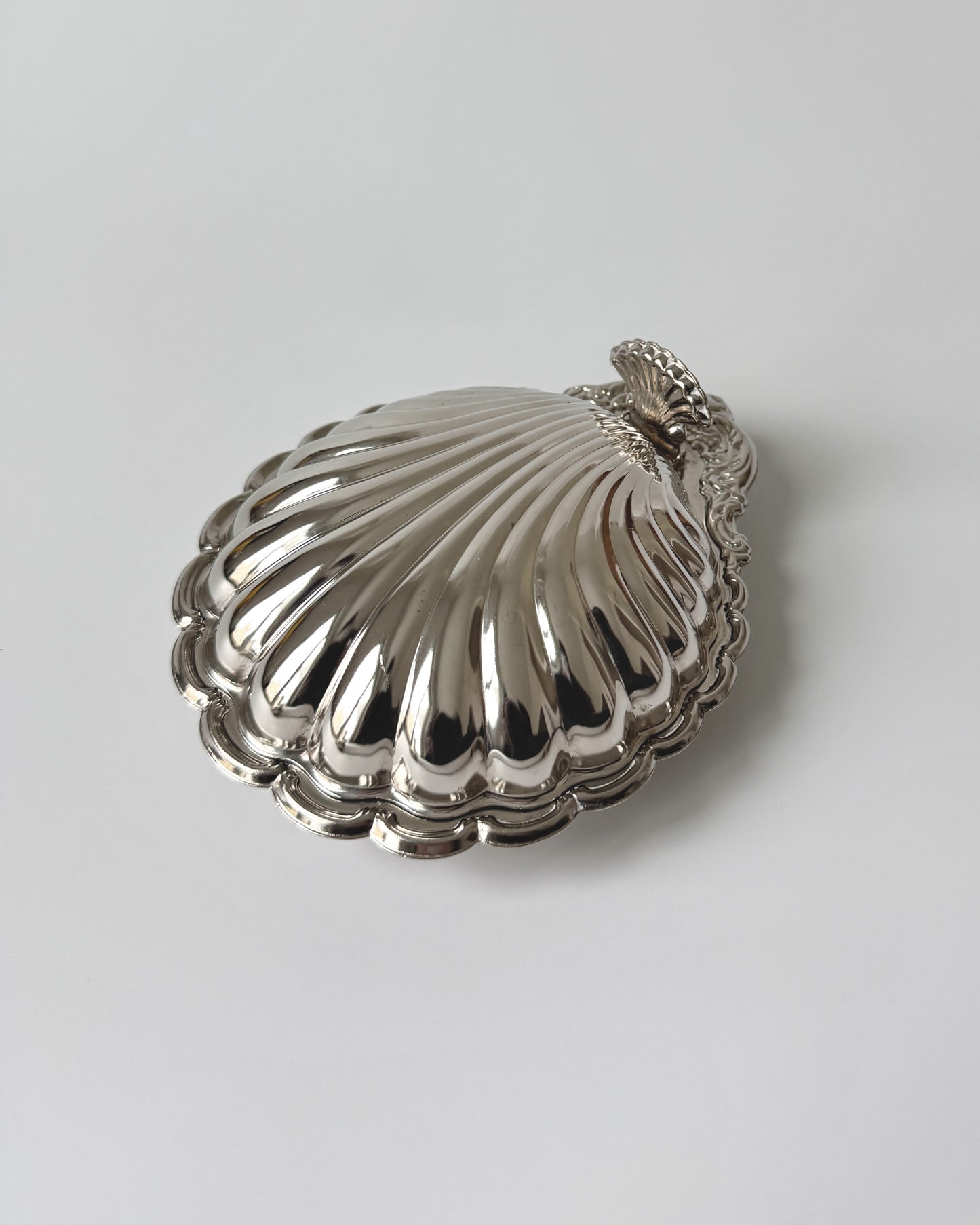A side profile of the sculptural clamshell serving dish, showcasing its elegant 1970s Hollywood Regency silhouette and deep-set silver-plated curves.