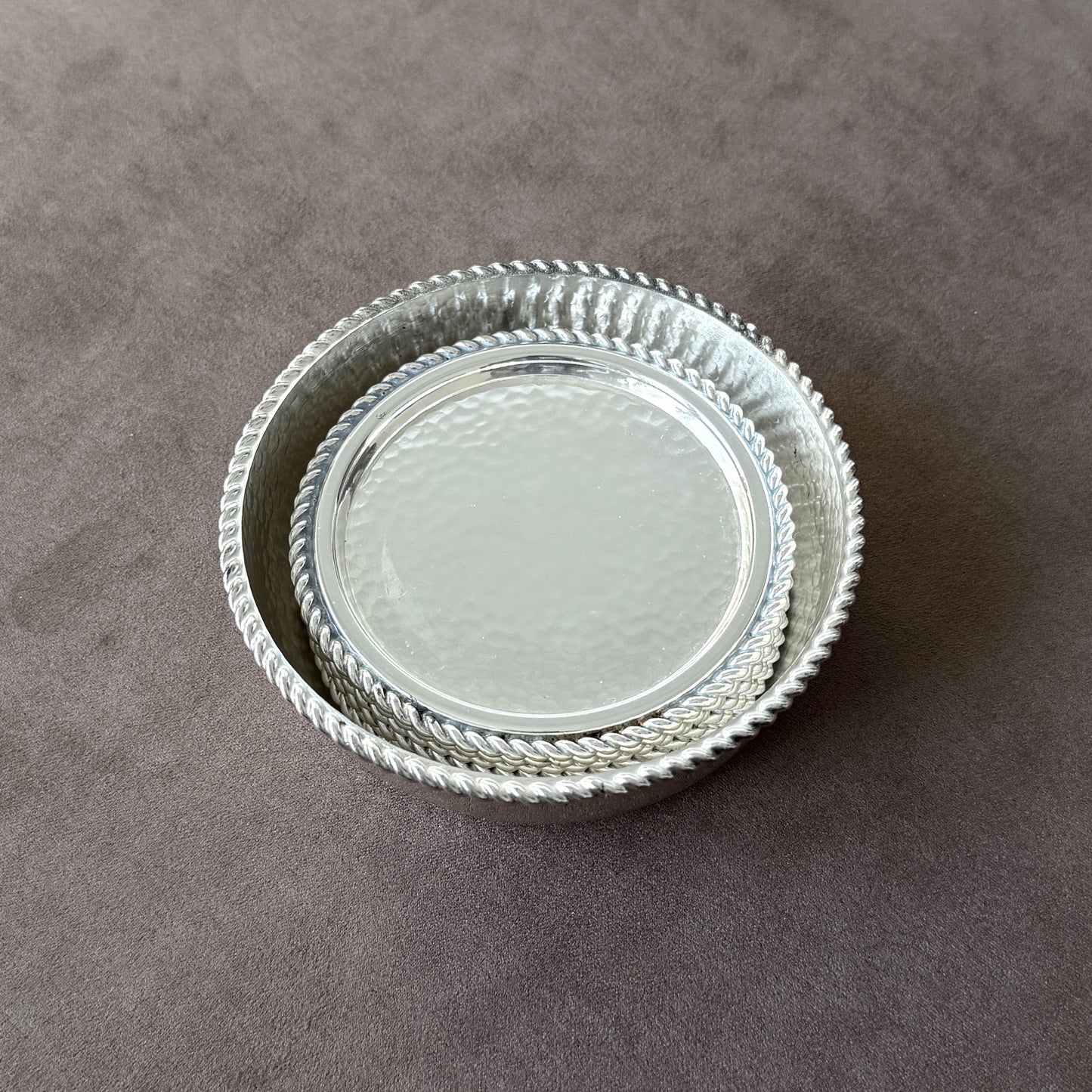 The large hammered silver wine bottle coaster serving as a caddy for the six smaller coasters, showcasing the elegant storage design and rope rim detail.