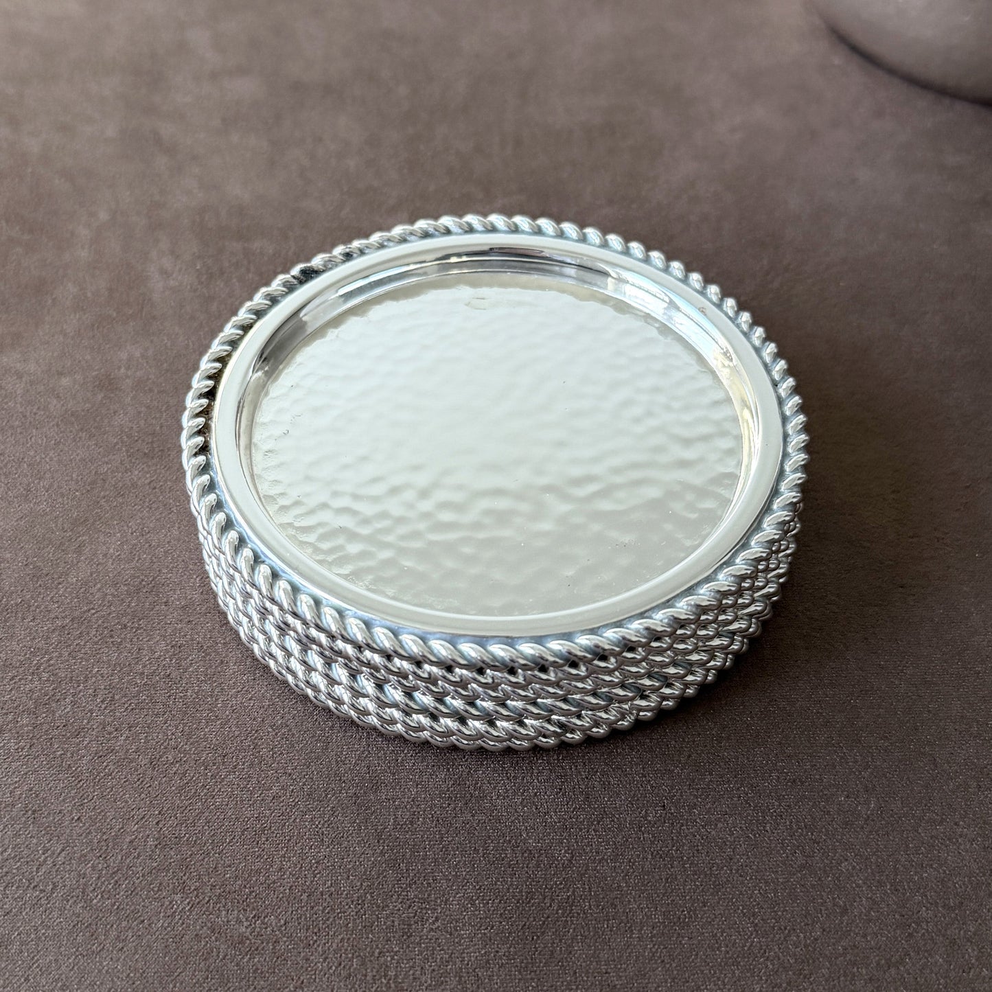 Six vintage silver-plated drink coasters arranged on a brown surface, highlighting their mirror-bright finish and hand-finished dimpled texture.