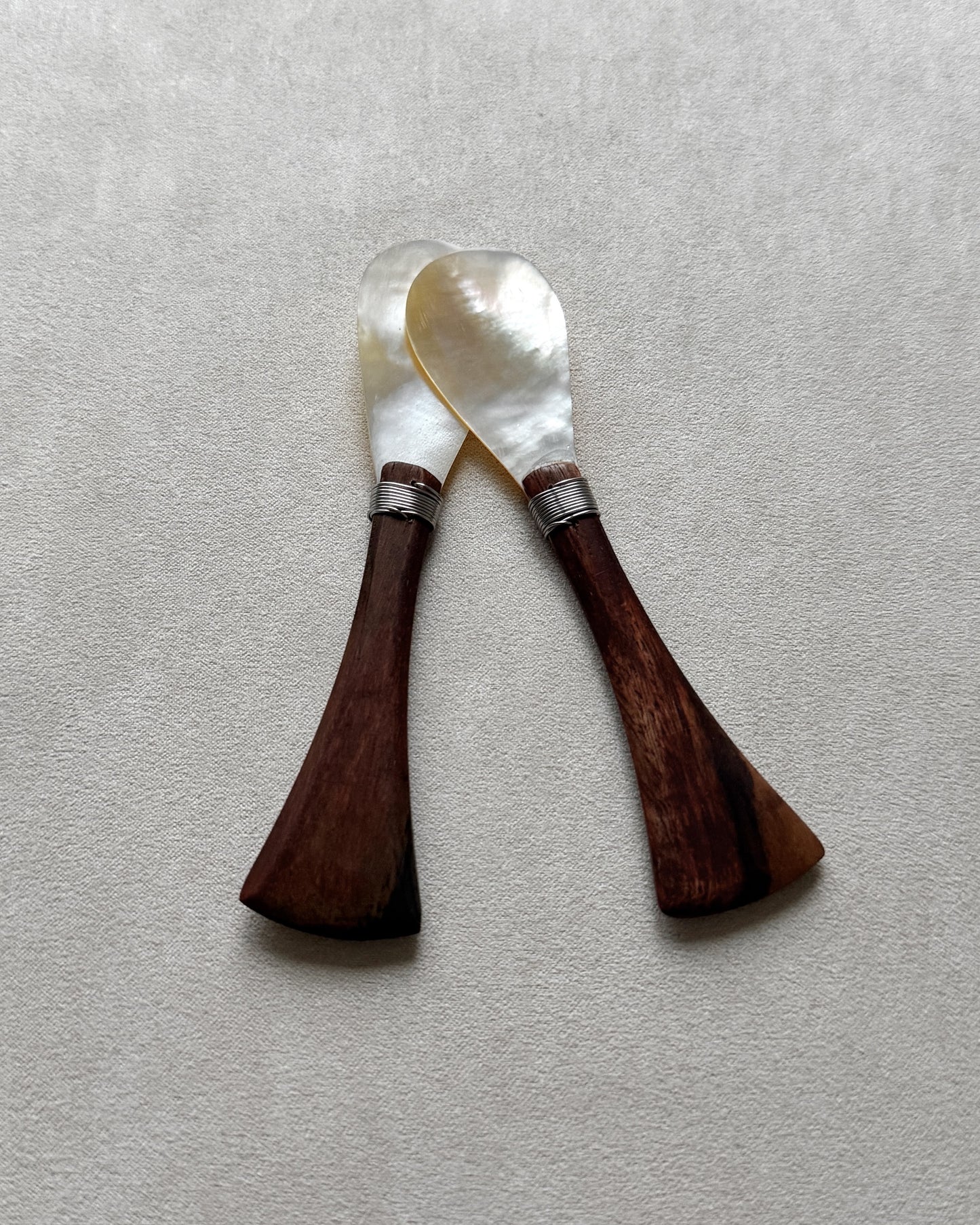 A zoomed-in shot of two spoons showing the high-quality metal fastening, the rich grain of the teak wood, and the luminous shimmer of the shell bowl.