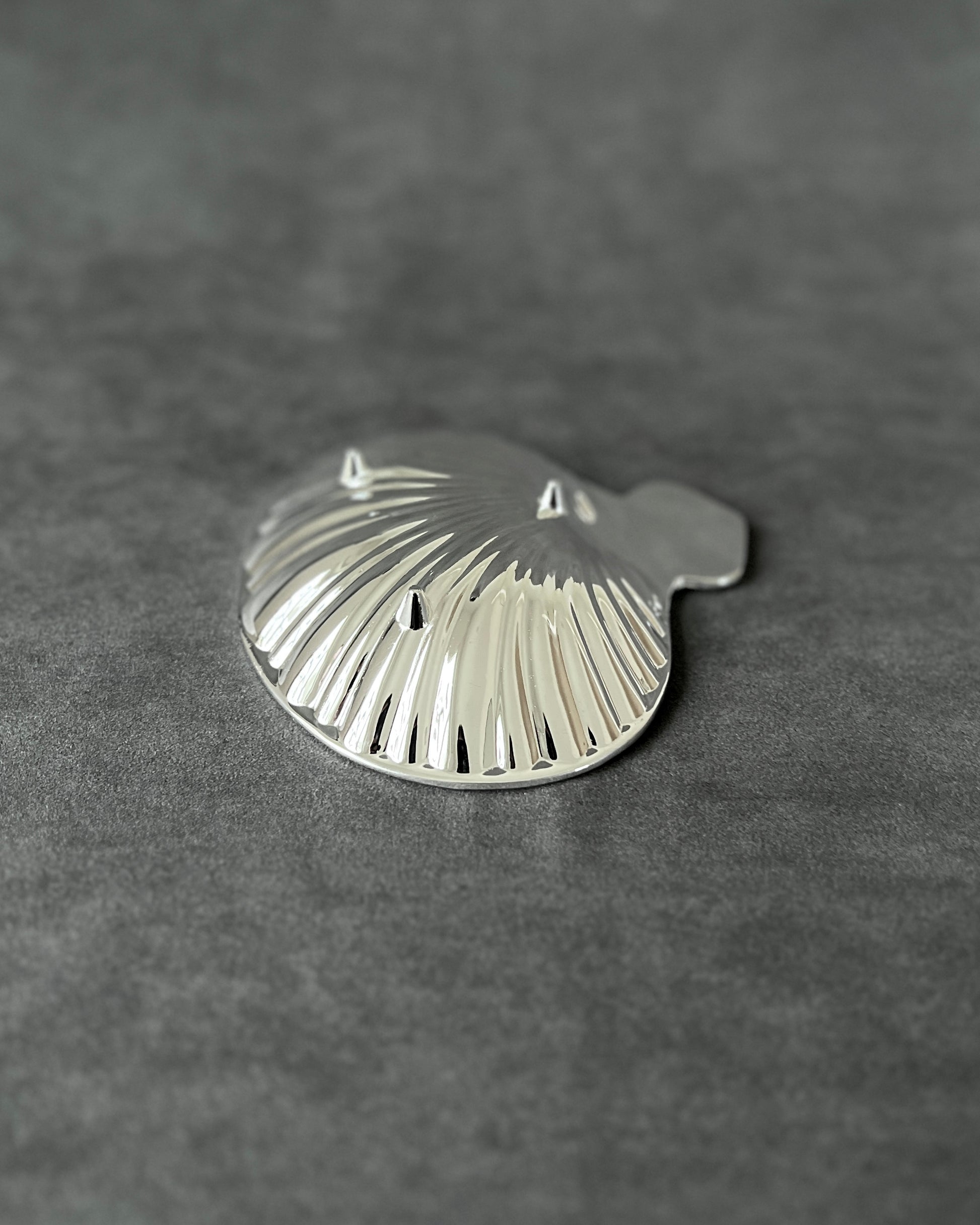 Side view of vintage silver shell dish, capturing its curved profile and reflective scallop design from a low angle.