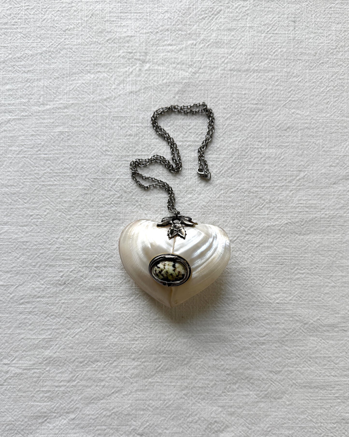 Close-up of the handmade mother-of-pearl heart box, highlighting the smooth, iridescent natural shell texture and vintage metal hardware.