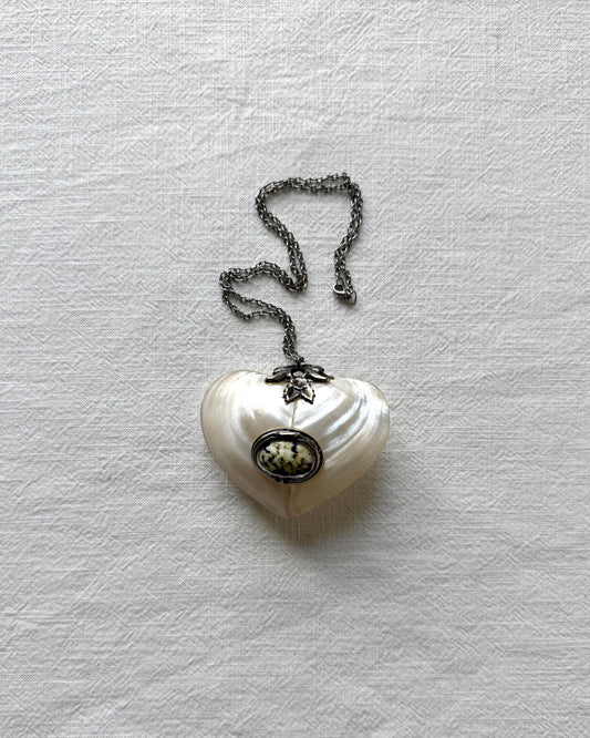 Close-up of the handmade mother-of-pearl heart box, highlighting the smooth, iridescent natural shell texture and vintage metal hardware.