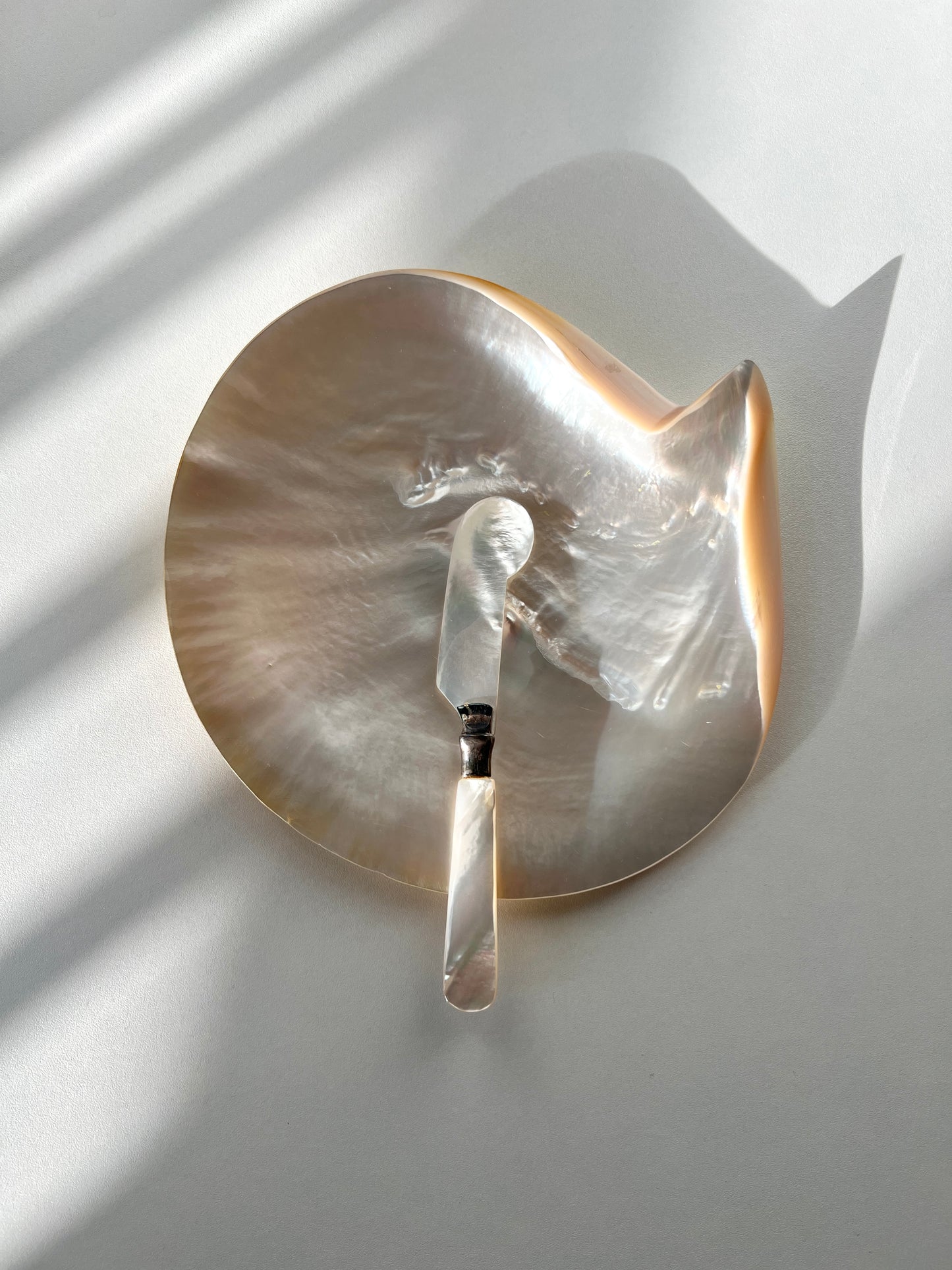 The matched vintage mother-of-pearl caviar knife shown on its own, highlighting its polished pearl handle and delicately shaped blade.