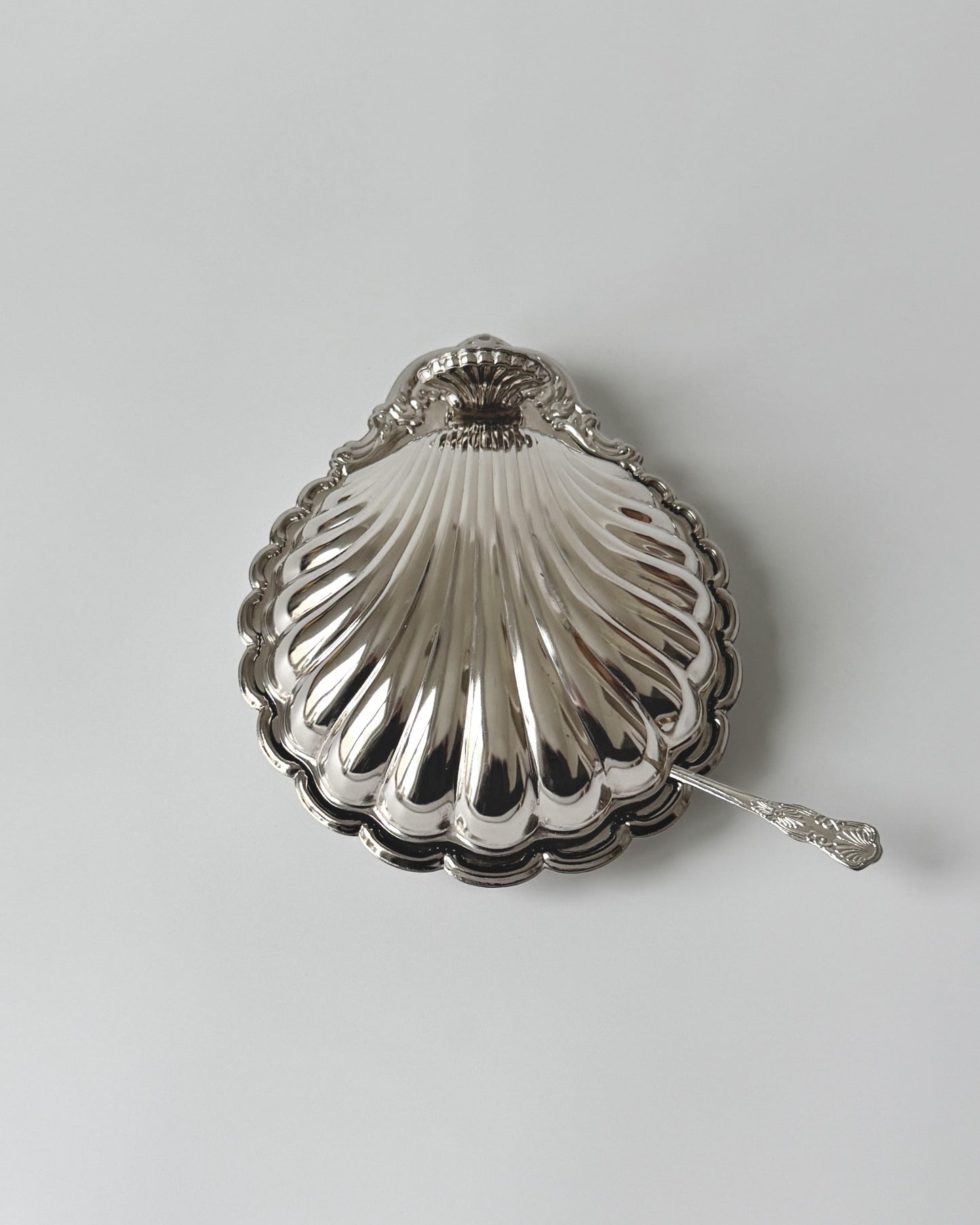 A complete vintage 1970s silver-plated clam shell serving dish with its original clear glass insert and matching coastal spreader knife on a white background.