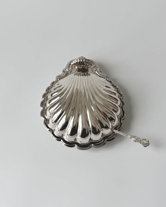 A complete vintage 1970s silver-plated clam shell serving dish with its original clear glass insert and matching coastal spreader knife on a white background.